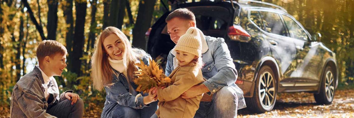 Une famille admire les feuilles d’automne en forêt, une voiture étant garée derrière eux.